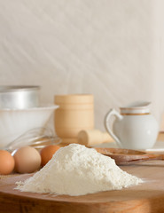 Fototapeta na wymiar white wheat flour and raw chicken eggs to prepare the dough and kitchen utensils against a white wall. Concept of rustic kitchen, selective focus. Copy space. Free space for text