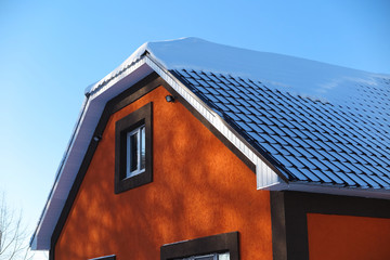 Modern roof covered with tile effect PVC coated metal roof sheets with snow against a blue sky