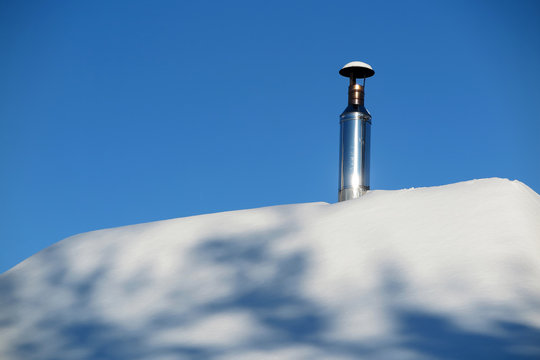Modern steel chimney of a Russian sauna covered with snow against a blue sky