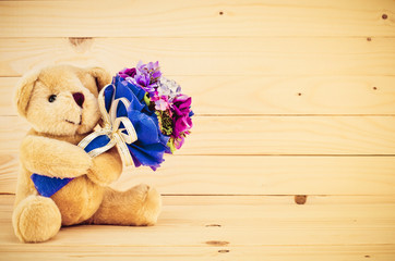 Bear with bouquet in hand rest on wooden wall.