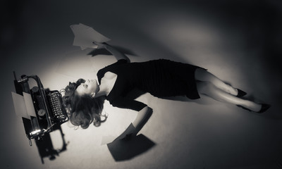 Young woman in black dress lies near a typewriter.