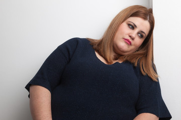 sad overweight woman leaned against a wall