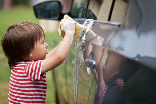 Cute young boy washing car with sponge in a garden