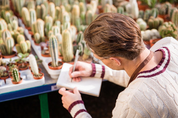 Male gardener making notes about condition of cactuses