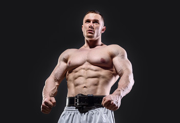 Fototapeta na wymiar Muscular man in with lifting belt posing over dark background