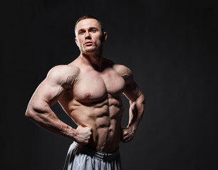 Fototapeta na wymiar Strong muscular man posing in studio over dark background
