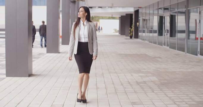 Beautiful confident Caucasian business woman with grin walking outdoors near office building