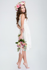 Beautiful woman in white dress and roses wreath standing barefoot