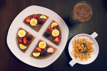 Pancake cut in four parts decorated with fruits, glass of cold coffee drink and bowl youghurt granola