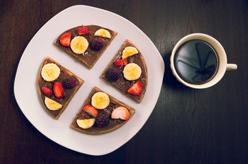 Fototapeta na wymiar Pancake cut in four parts decorated with fruits, flanked cup of coffee
