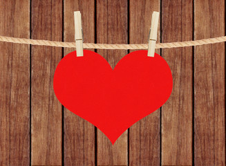 red heart hang on clothespins over wooden planks background