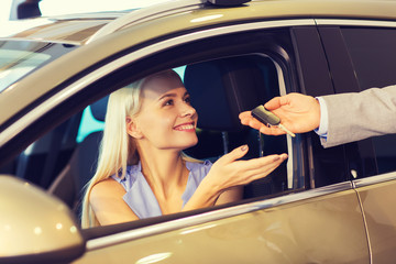 happy woman getting car key in auto show or salon