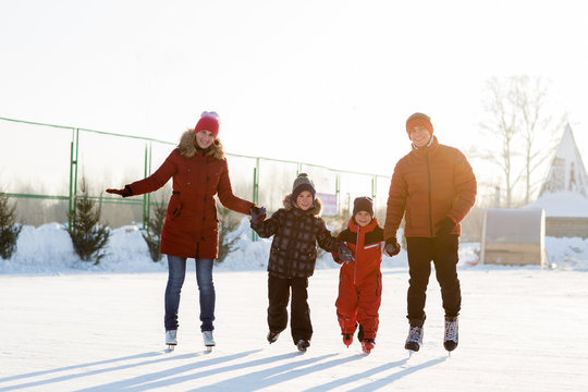 Happy Young Family Skate At The Rink In The Winter. Beautiful Family Walking And Playing On The Ice In Winter.