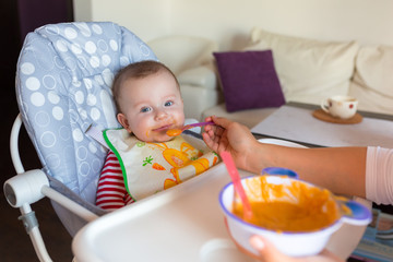 Baby boy eating carrot puree on the high chair
