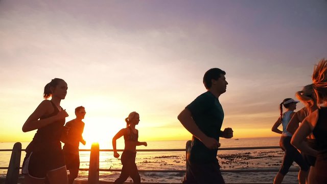 Running club running along sea promenade in the sunset. Young people running on the road along the sea in evening. 
