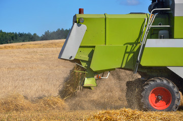 Working harvester on the yellow field with hay. Close-up of the back side.