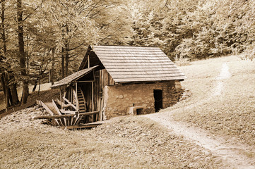 Old stone and wooden water mill in rural setting with vintage desaturated effects.