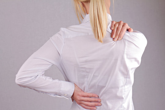 Woman with neck / back pain. Business woman rubbing her painful back close up. Pain relief concept