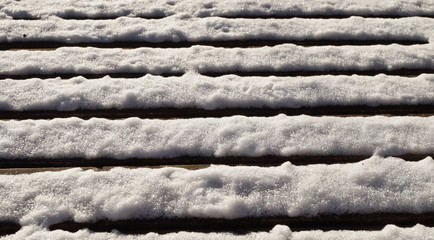 White snow fallen on the horizontal slates of a wooden park bench