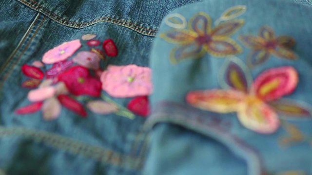 Close up of blue denim jeans girl clothes with beautiful floral decorations and colorful stitches. Structure of denim textile decorated with needlework and fabric applique. Beautiful denim background