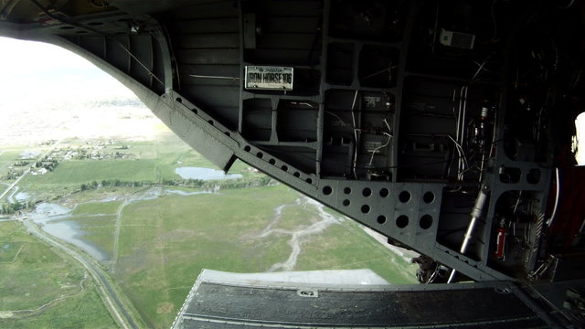 Time lapsed, ground below can be seen through the back hatch as the chopper flies over green fields and some homes.