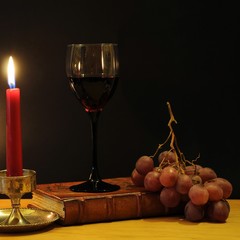 Glass of red wine with grapes, candle and old book