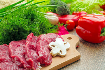 fresh vegetables, mushrooms, champignons,cabbage, pepper, cherry, greens on a wooden board with crude stakes of meat of veal, spices, close up, the top view