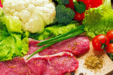 fresh vegetables, cabbage, pepper, cherry, greens on a wooden board with crude stakes of meat of veal, spices, close up, the top view