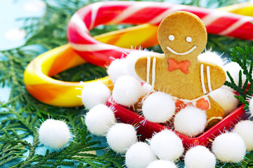 Christmas, traditional ginger gingerbread in the form of the little man of handwork, close up against from fir-tree branches and striped caramel