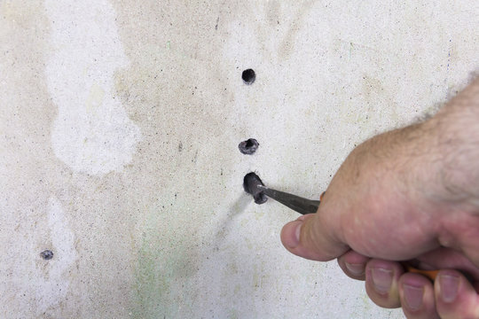 DIY, close up of man's hand removing an old wall plug (rawlplug)  from an interior wall  using pliers while renovating and redecorating a house.