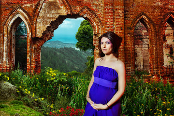 Beautiful pregnant woman is standing at ruined vintage castle 