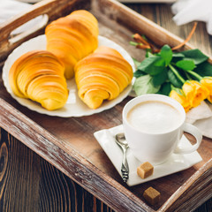 Coffee, croissant and flowers on tray on a wooden table
