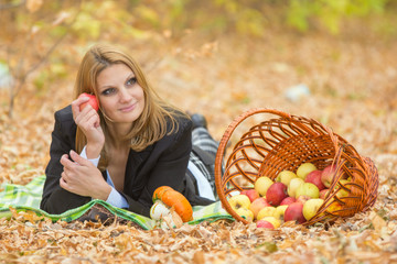 Young beautiful girl lies on the on the foliage in the autumn forest and dreaming holding an apple and looking to the right