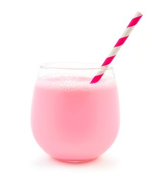 Strawberry milk in a glass tumbler with striped paper straw isolated on a white background