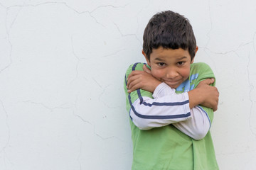 Shy gypsy child boy expressing poor unsure feelings lean against white wall