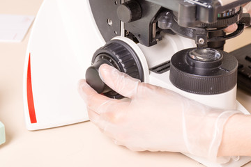 Medical or scientific researcher using a microscope in laboratory environment with test tubes and equipment