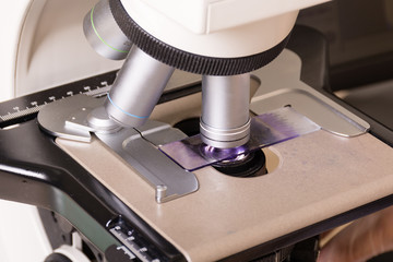 Medical or scientific researcher using a microscope in laboratory environment with test tubes and equipment