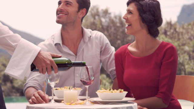 Waiter pouring red wine in glass for couple