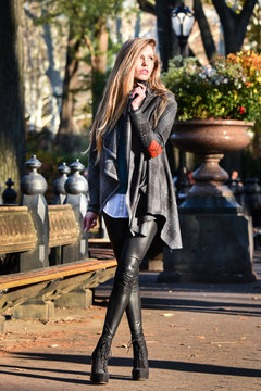 Beautiful blonde model wearing stylish coat and leggings posing at Central Park during fall fashion photo shoot.