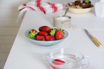 Fresh strawberries in a transparent bowl on the white table