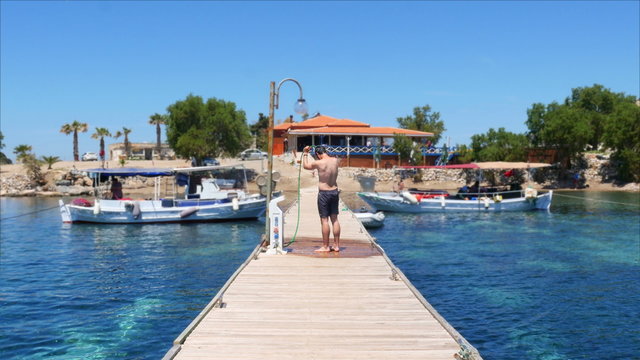 happy man showering on wooden pier at beach after swimming