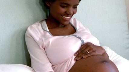 Pregnant woman sitting on bed touching her belly - Powered by Adobe