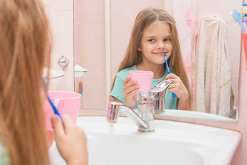 Girl standing with a toothbrush and a glass in the bathroom