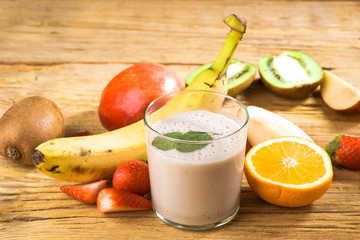 Natural banana smoothie surrounded by fruit on wooden base