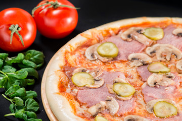 closeup Tasty pizza with mushrooms, ham and pickles on a black b