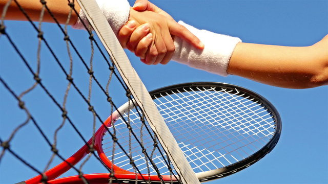Girl tennis players shake hands over the tennis court net