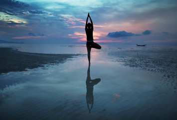 Silhouette of a young woman practicing yoga on the beach at sunrise