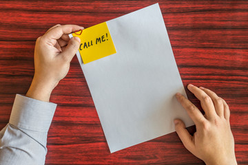 Hands holding blank page with yellow note attached by heart shaped paper clip.