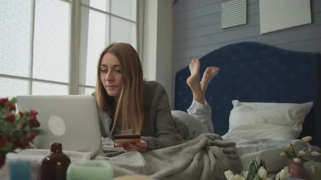 Blond in bed with a laptop spends money.