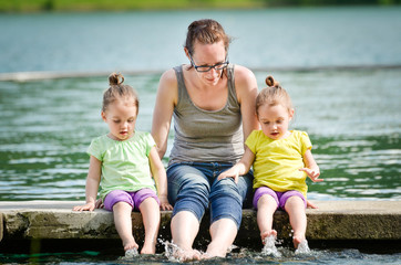 Fototapeta premium Mother and little children twin girls are playing on a lake